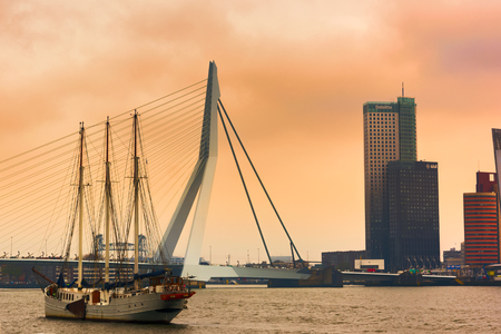 ROTTERDAM, NETHERLANDS - APRIL 13, 2018: View on the Erasmus Bridge with vessel on foreground and cityscape during sunset, also called The Swan, on the Maas river in Rotterdam.のeditorial素材