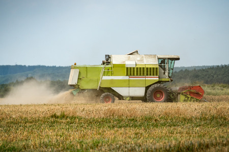 combine harvester that is harvesting wheat with dust straw in the airの写真素材