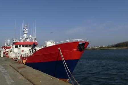 Red fishing boat moored alongside the wharf at the fishing harbor of Lorient, Brittany France. Horizontal view from bowの写真素材