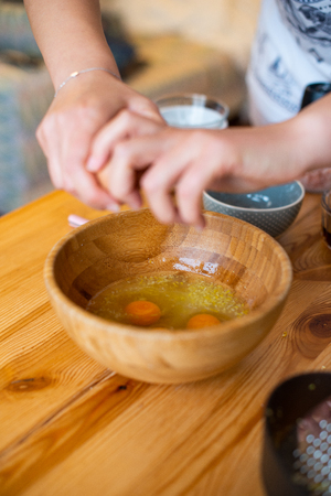 breaking an egg into a wooden bowl, woman hands shown, concept for cooking and bakingの写真素材
