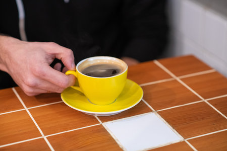 filter coffee in a yellow cup, held by man hands. black coffee with man hands shown.
