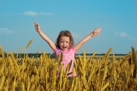 Happy girl in wheat field with her hands upの写真素材