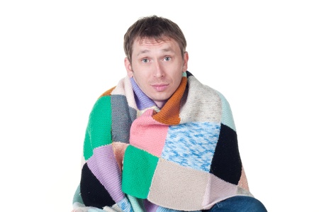 man wrapped in a warm blanket and scarf shivering from the cold on white backgroundの写真素材