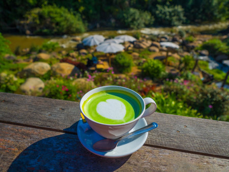 a cup of hot milk green tea is on wood rail at Himnam cafe, chiengdao, Thailand, with beautiful...