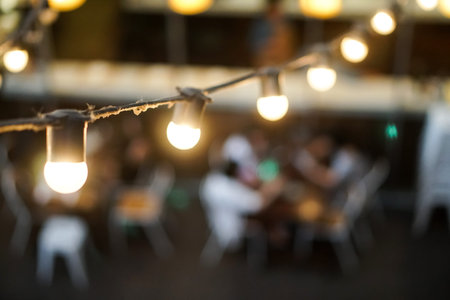 light bulb hang on wire outdoor restaurant blurred people background