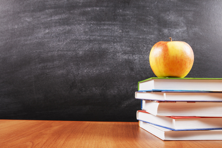 A Stack Of Books And An Apple On Blackboard Background With