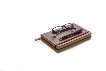 Glasses and pen ready to write on top of brown agenda with white background