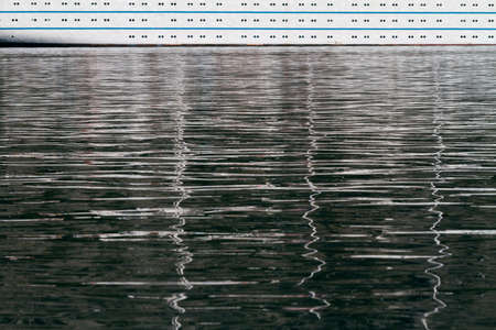 Part of cruise liner board with illuminators reflecting on a sea surface.の写真素材