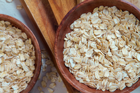 Whole oat flakes in wooden bowls on a light cement background, tinted