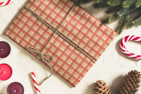 Christmas gift wrapped in checkered craft paper with candles and decorations on a rough surface,...