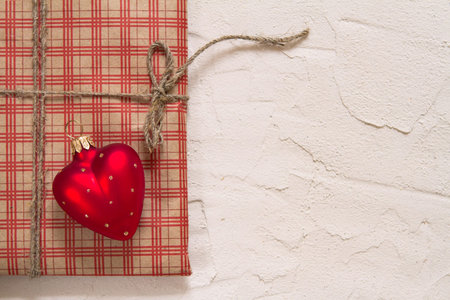 Christmas gift wrapped in checkered craft paper with candles and decorations on a rough surface,...