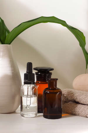 Home spa, cosmetic oil in a bottle, wooden bowl on a white table with a plantの写真素材