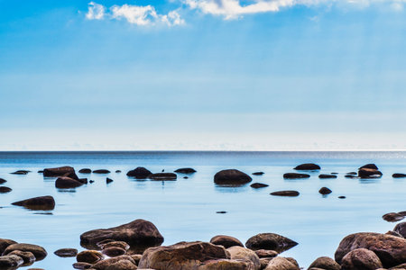 Stone Boulders in the Calm Waves of the Azure Ocean Against a Blue Sky with White Clouds.