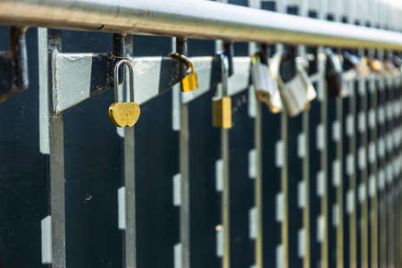 Heart-Shaped Padlock Hanging on Rails Among Other Variegated Padlocksの写真素材