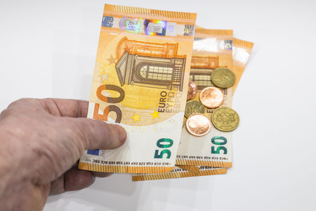 Male hand holding 50 Euro note and coins in the background