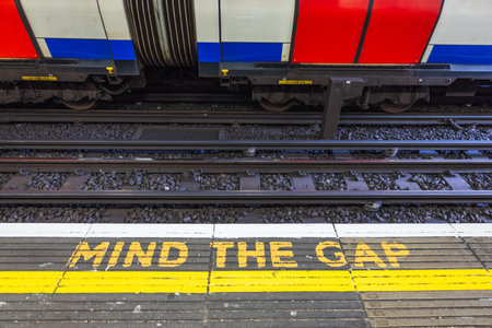 Iconic MIND THE GAP Sign on London Tube Platform, Safety Message and Trainの写真素材