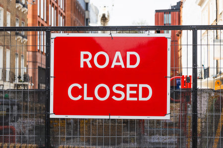 Road Closed warning sign on metal fence at busy city construction site
