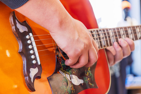 Musician strumming bright orange acoustic guitar, showing hand technique and fret detail
