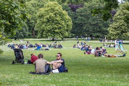 People relaxing on the grass in a sunny city park. London, UK, 8 June 2024のeditorial素材
