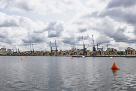 Historic cranes along the waterfront at London Docklands under clouds. London, UK, 29 June 2023