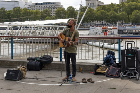 Street musician playing acoustic guitar on a city riverside promenade. London, UK, 23 July 2023のeditorial素材