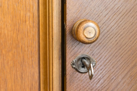 Part of an old wooden door with round wooden handle and metal key in a keyhole closeupの写真素材