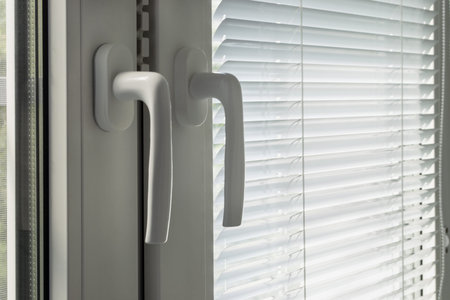 Part of closed white window with closed blinds and handles closeup