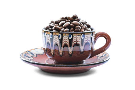 Cup on a saucer full of coffee beans isolated over whiteの写真素材