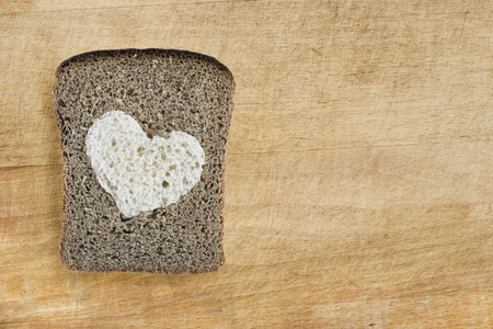 Piece of rye bread with white heart on wooden board as a backgroundの写真素材