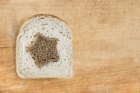 Piece of wheaten bread with brown star on wooden board as a background