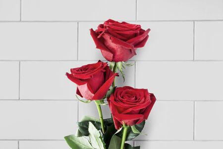 Bouquet of three red roses over brick wall as a backgroundの写真素材
