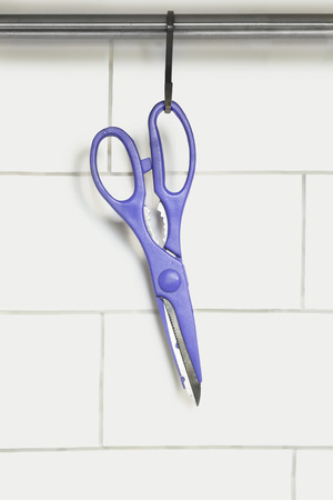 Purple scissors hanging against white brick wallの写真素材