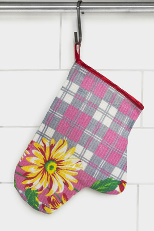 Textile colorful oven-glove hanging against white brick wallの写真素材