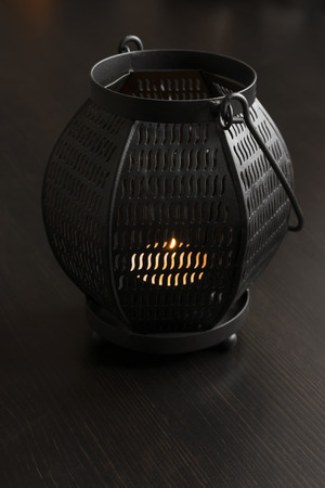 Metal lamp with burning candle inside on dark wooden deskの写真素材