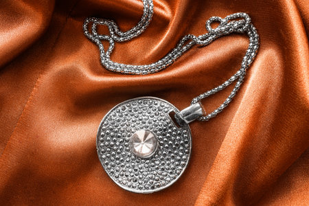 Medallion on a silver chain on golden satin as a backgroundの写真素材