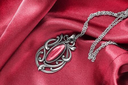 Silver vintage pendant on red silk as a backgroundの写真素材