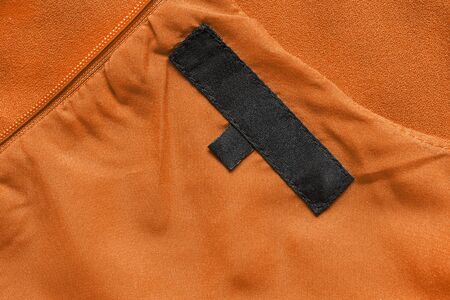 Black clothes label on orange silk as a backgroundの写真素材