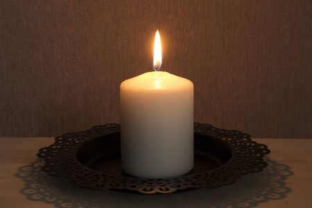 Single white burning candle on black dish closeupの写真素材