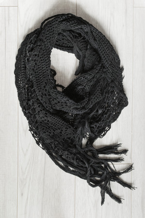 Black crocheted scarf with fringe on white wooden backgroundの写真素材