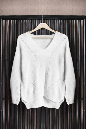 White knitted sweater on clothes rack hanging on black folding screenの写真素材