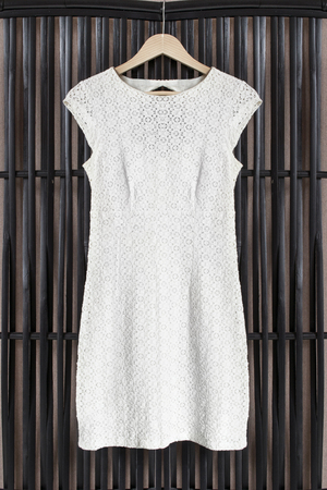 White lacy dress on clothes rack hanging on black rattan screenの写真素材