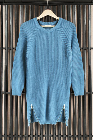 Blue knitted dress on clothes rack hanging on black bamboo screenの写真素材