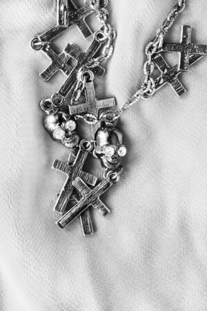 Chain with silver crosses and skulls on white silk as a backgroundの写真素材