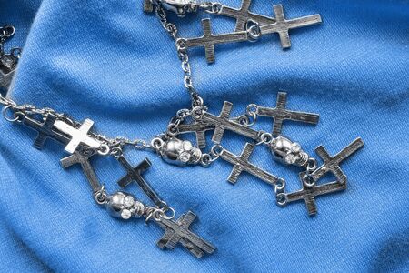 Silver chain with crosses and skulls on blue cloth as a backgroundの写真素材