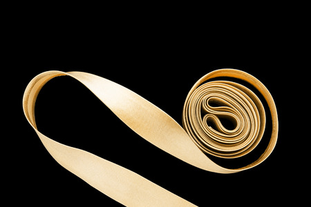 Rolled golden satin ribbon on black backgroundの写真素材