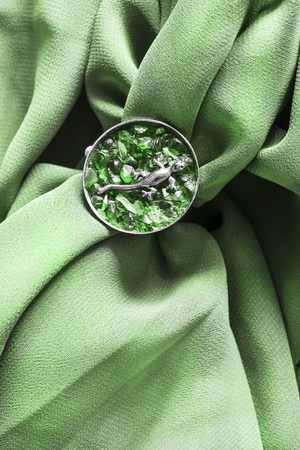 Emerald brooch with silver lizard on crumpled green silk as a backgroundの写真素材