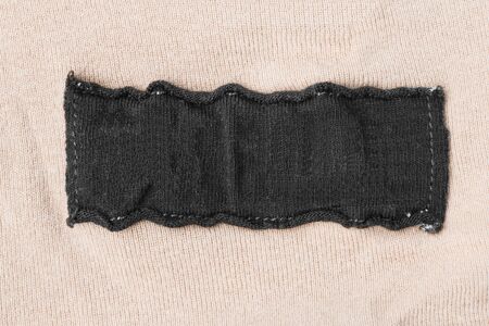Blank black clothes label on beige cloth as a backgroundの写真素材