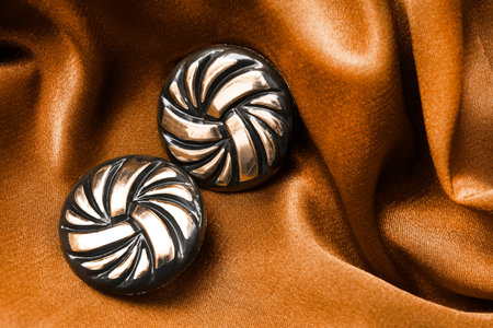 Pair of golden earrings on yellow crumpled satin closeup