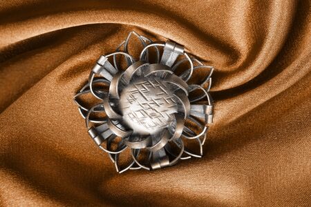Vintage bronze brooch on orange draped satin closeupの写真素材