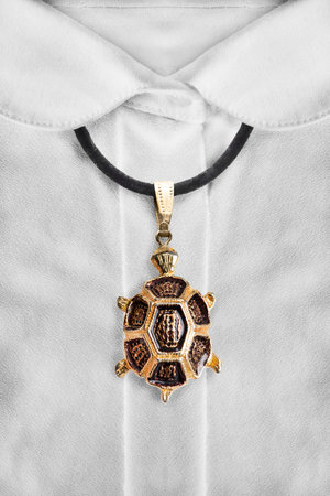 Gold turtle pendant on black lace over white blouse closeupの写真素材